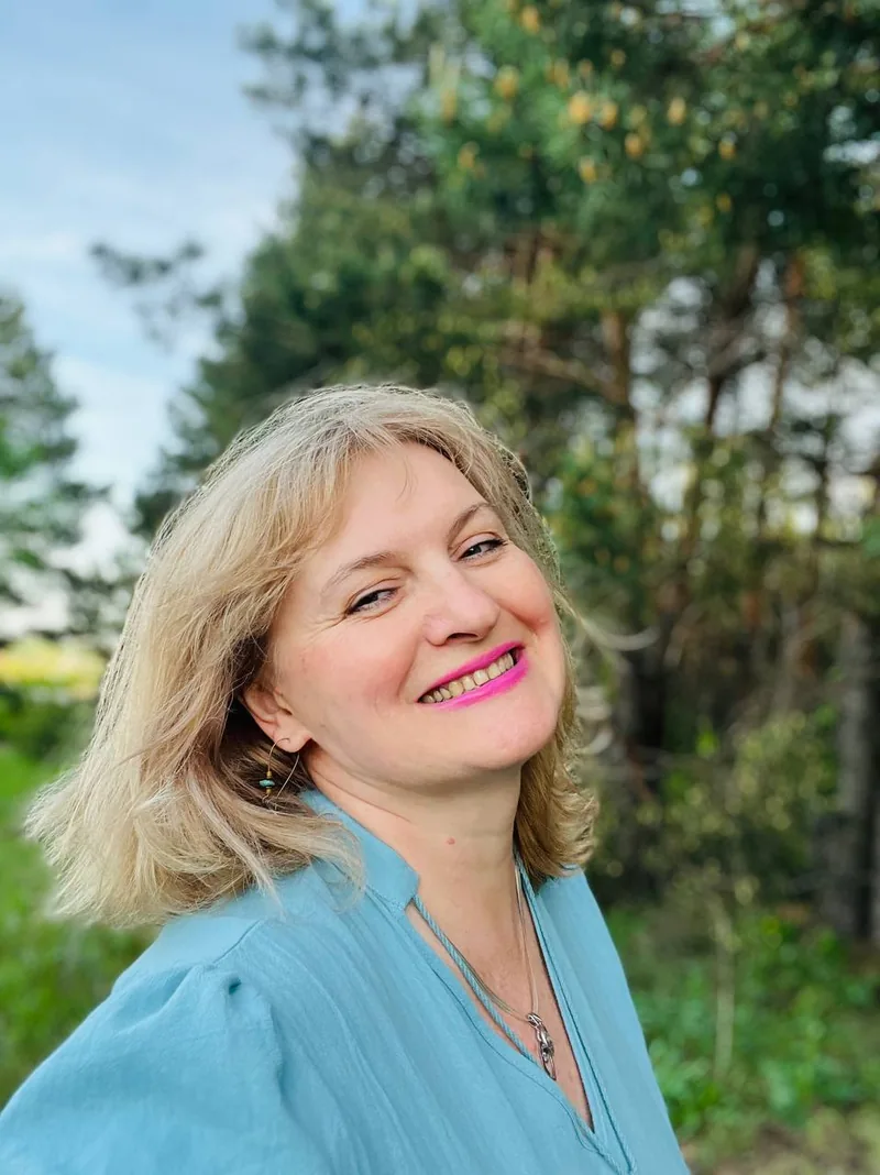 Елена Щербинина улыбается, в голубой блузе, на фоне сосен
